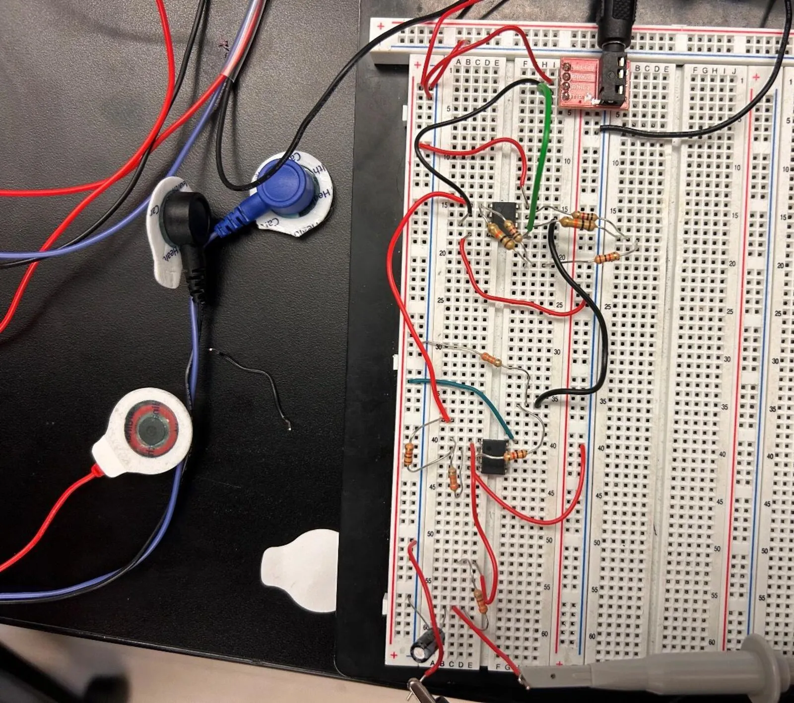 A breadboard with two op-amp chips and resistors wired up, next to three ECG electrode pads and their leads