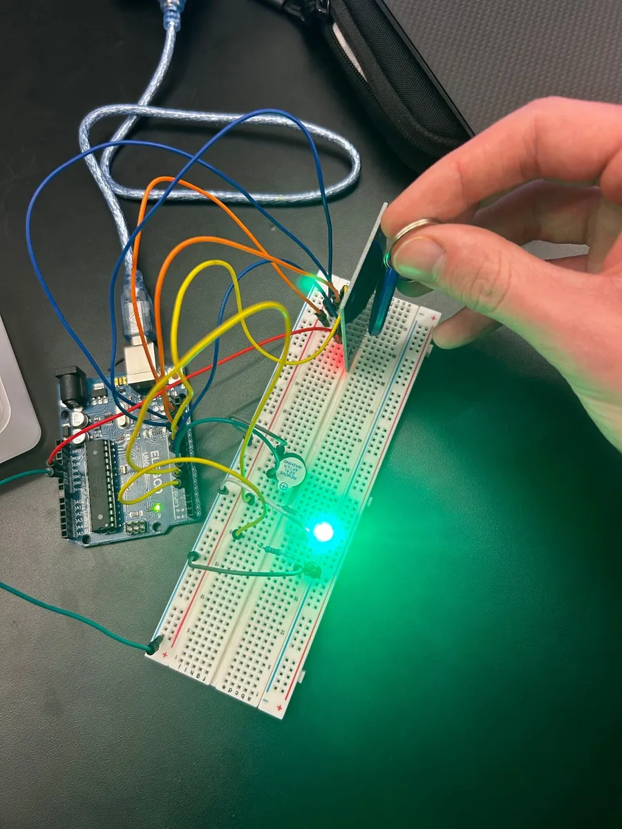 A hand holding a keyring up to the RFID reader while the green LED glows